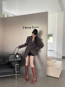 Κομψή γυναίκα με γκρι oversized σακάκι και κοκκινωπές καφέ ψηλές μπότες με τακούνι και στυλ