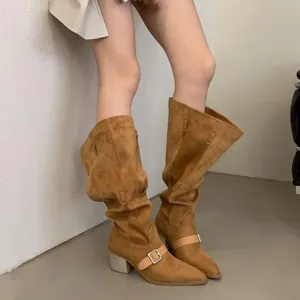 Detail view of fashionable brown suede slouchy Western boots with buckles on model legs.