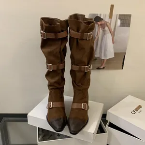 Close-up of brown suede slouch boots with triple buckle straps and pointed toe