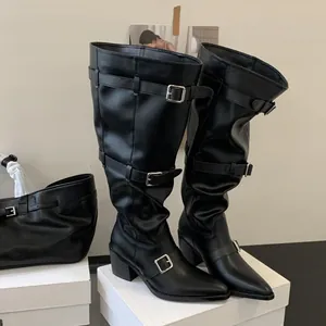 Close-up of black pointed-toe slouchy tall boots with metal buckle straps and chunky heels