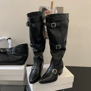 Close-up of black pointed toe slouchy boots with buckle straps and chunky heels
