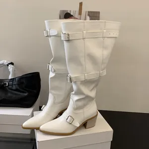 Detailed view of white pointy-toe slouchy boots with stylish metallic buckle straps.