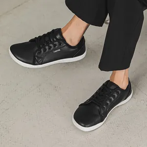 Detailed view of black leather wide toe box barefoot shoes on feet with white flat soles