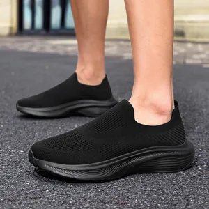 Close-up view of men's black breathable fly-knit slip-on sneakers worn on asphalt