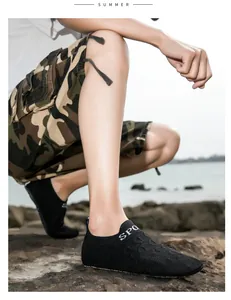 Dettaglio di una scarpa da wading nera in maglia fly-knit indossata su una spiaggia rocciosa