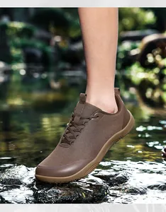 Close-up of brown wide-toe barefoot hiking shoes worn on a rocky stream bank