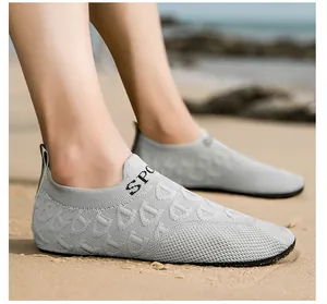 Dettaglio ravvicinato di scarpe da scoglio in maglia grigia indossate su una spiaggia.