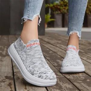 Detail view of breathable grey Flyknit slip-on sneakers with thick white soles on wooden floor.