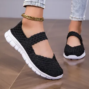 Detail view of black woven elastic strap sandals with lightweight white soles on wooden floor