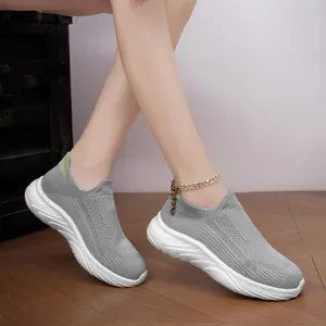 Close-up of grey breathable knit slip-on sneakers worn on wooden floor with gold anklet