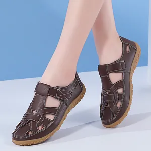 Detailansicht von stilvollen braunen flachen Sandalen mit weißen Kontrastnähten und Ausschnitten