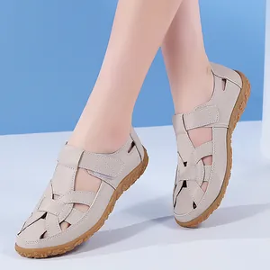 Nahaufnahme von beigefarbenen flachen Damen-Sandalen aus Leder mit Lochmuster