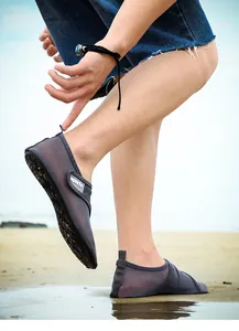 Close-up view of grey breathable mesh beach swim shoes worn on sand at the beach