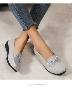 Close-up van grijze dames loafers met een decoratieve strik en witte stiksels.