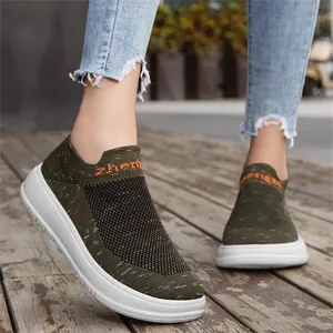 Close-up of green fly-knit slip-on sneakers with breathable mesh on a wooden path