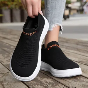 Detail of black breathable fly-knit slip-on sneakers with thick white soles on wood.