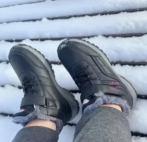 Close-up of black winter snow boots with warm grey fur lining worn on a snowy wooden bench