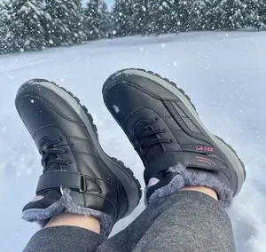 Close-up of black waterproof winter snow boots with warm faux fur lining on snow