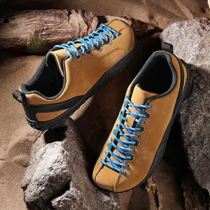 Gros plan de chaussures de randonnée pieds nus beiges avec lacets bleus sur du sable.