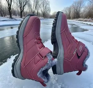 Close-up of warm maroon snow boots with grey faux fur lining on a frozen river background.