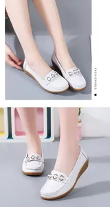 Detailopname van witte leren casual wedge loafers met decoratieve gouden kettingaccenten.
