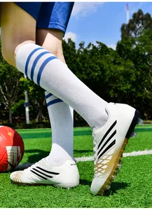 Action-Detailansicht von weißen Jugend-Fußballschuhen mit goldenen Akzenten auf Rasenplatz