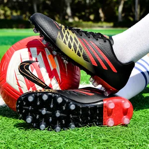 Jugend-Fußballschuhe mit gold-roten Mustern auf grünem Rasen mit einem Fußball