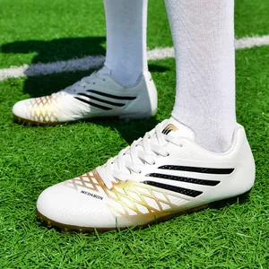 Weiße und goldene Fußballschuhe für Jugendliche mit Turf-Stollen auf Rasenfläche