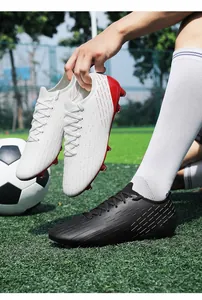 Professional low-top turf soccer cleats held by player on green football field.