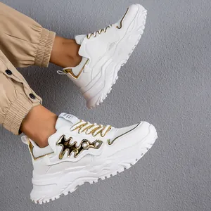 Primo piano di sneakers chunky bianche con accenti dorati e spessa suola a piattaforma