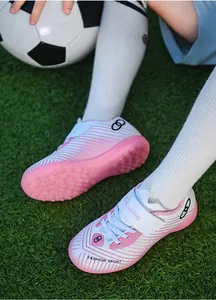 Close-up detail of pink and white children's turf soccer shoes on artificial grass field
