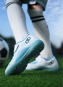 Close-up of blue and white children's turf soccer shoes with non-slip rubber studs on grass