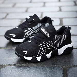 Side view of black boys' running shoes with white fashion accents on stone tiles