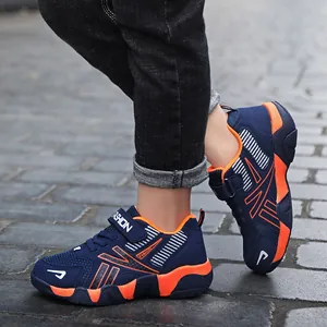 Detailed view of boys' breathable navy and orange mesh sneakers on stone pavement