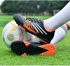 Detailopname van ademende zwart-oranje voetbalschoenen met rubberen noppen op gras