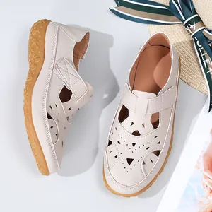 Close-up of beige hollow-out flat sandals with floral perforations and velcro strap.