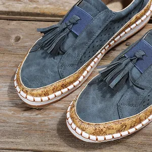 Gros plan de mocassins bleus avec détails de glands et bordure en liège sur une table en bois.