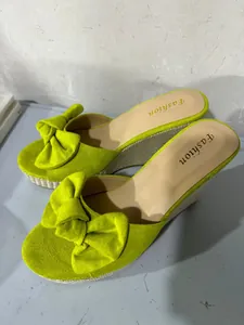 Close-up detail of lime green wedge sandals featuring a large decorative bow on the toe