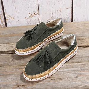 Mocassins verts foncés avec glands et détails perforés sur fond de bois rustique.