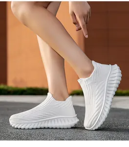 Detailed side view of comfortable white fly-knit slip-on sneakers on a person's feet