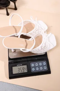 White lace high-heeled sandal being weighed on a digital scale, showing 359.4 grams