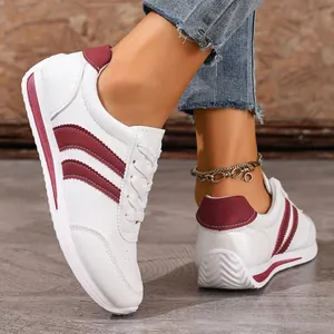 Close-up of white casual sneakers with maroon stripes and white laces on model feet