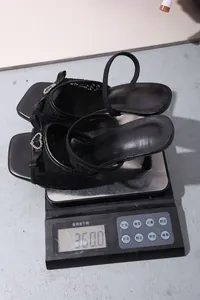Detail showing a pair of black lace high-heeled sandals weighing 360 grams on a digital scale