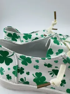 Close-up detail of white canvas shoes with green shamrock pattern and white laces