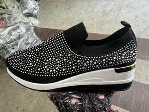 Detalle de zapatillas de cuña negras con pedrería, suela de plataforma blanca y sin cordones.
