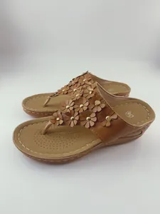 Vista ravvicinata di sandali marroni con zeppa, fiori in pelle 3D e borchie dorate