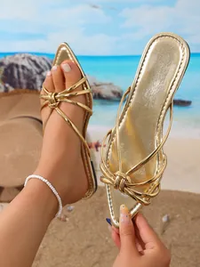 Dettaglio ravvicinato di eleganti sandali dorati a punta con design a nodo sulle fasce