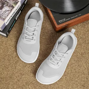 Top view of light gray wide-toe barefoot sneakers on a textured rug near a turntable