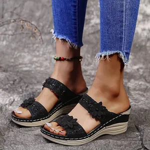 Detail of black wedge slippers with flower rhinestone accents on stone background