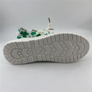 Bottom view of white sneakers featuring green clover pattern and textured rubber sole
